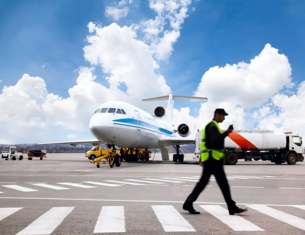 Man walks across a crosswalk on a tarmac in front of a passenger plane
